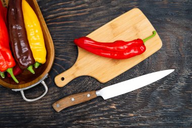 Kesme tahtasında bıçakla taze çiğ tatlı biber. Pişirmeye hazır. Koyu ahşap masa, üst manzara..