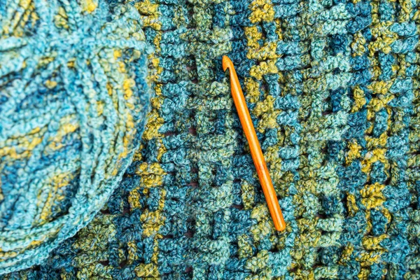 Crochet hook on a seamless knitted bedspread. The repeating texture of a hand knitted bedspread. Colored knitted background. Space for text.