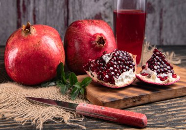 Olgun nar, yarım sulu nar suyu ve sağlıklı nar suyu kesme tahtasındaki bir bardakta, yan görünüşte, koyu renkli arka planda..