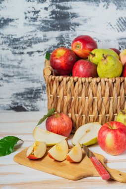 Beyaz bir masada taze armut ve elma hasadı olan sepet. Kesme tahtasında dilimlenmiş armut ve elmalar. Metin için boşluk