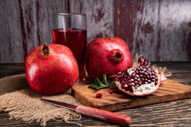 Olgun nar, yarım sulu nar suyu ve sağlıklı nar suyu kesme tahtasındaki bir bardakta, yan görünüşte, koyu renkli arka planda..