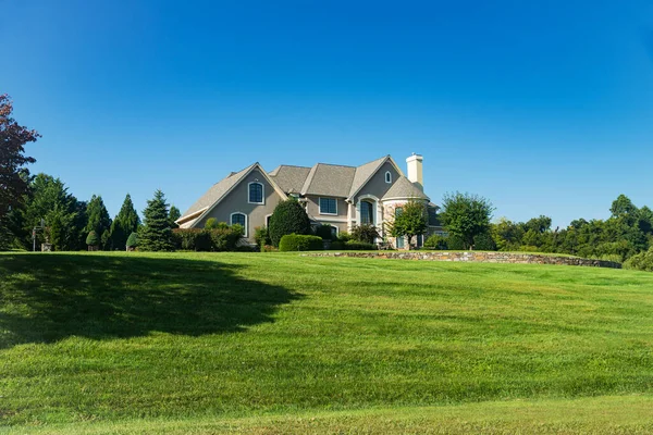 Large modern stone house on a hill with a huge green lawn. Country two-story house. Blue sky on a summer day.