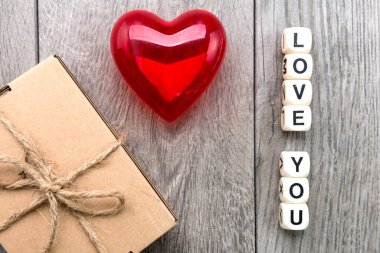 Gri arka planda kırmızı kalp. Bir kutuda hediye ve tahta küplerden bir yazı Seviyorum seni.