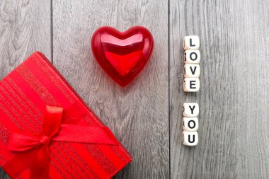 Bir kutuda hediye ve tahta küplerden bir yazı. Seni seviyorum. Gri arka planda kırmızı kalp.