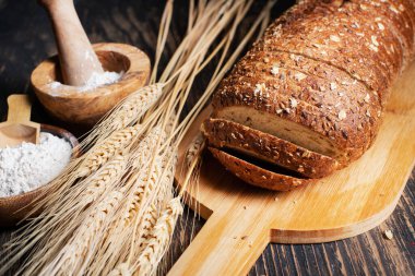 Bir somun çavdar ekmeği, buğday kulakları ve bir kase un. Yakın plan..