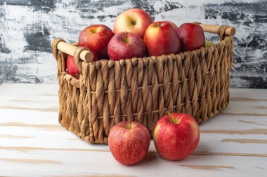 Olgun, sulu elmalar hasır sepetin içinde, beyaz tahta bir masada..