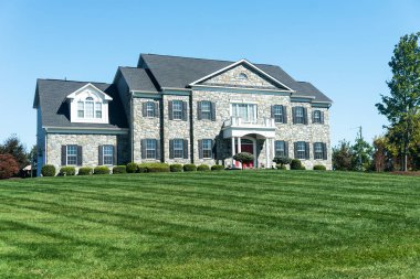 Taş cepheli iki katlı bir ev. Garaj ve yeşil çimenler.