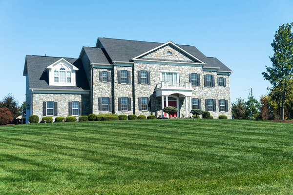 Двухэтажный дом с каменным фасадом. Гараж и зеленая лужайка.