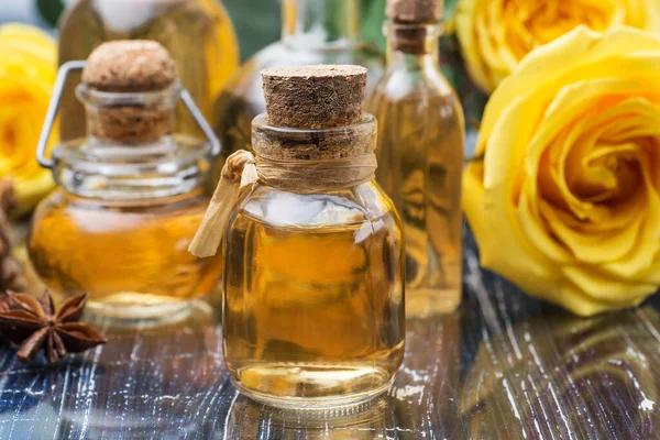 Cosmetic and aromatic rose oil in bottles. Yellow roses on a blue table.