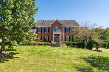 Large brick house with a green lawn. Sunny summer day, cloudless sky.