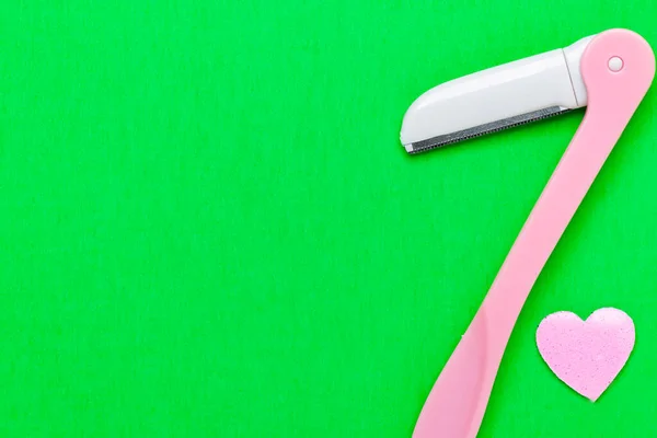 Pink disposable razor blade on green background. Single use razor blade. Disposable shaving razor. Body care. Space for text.