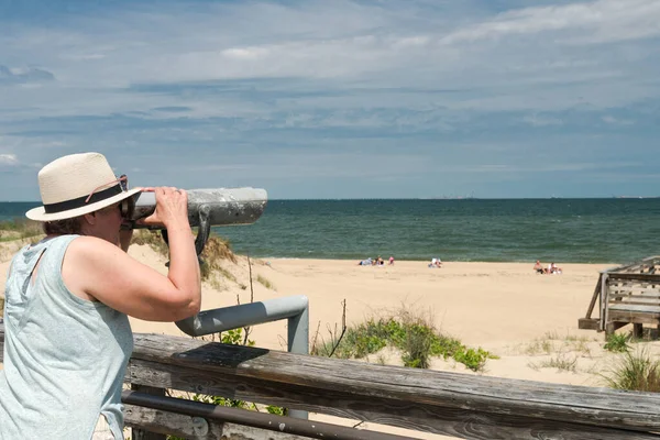 woman in hat looks through Coin binoculars at ocean. Seascape of the Atlantic Ocean on a summer day.