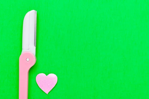 Pink disposable razor blade on green background. Single use razor blade. Disposable shaving razor. Body care. Space for text.