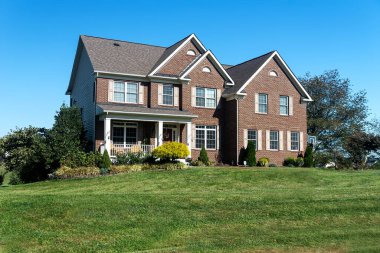 Luxurious brick house with a green lawn and trees at the entrance. Sunny summer day, cloudless sky.