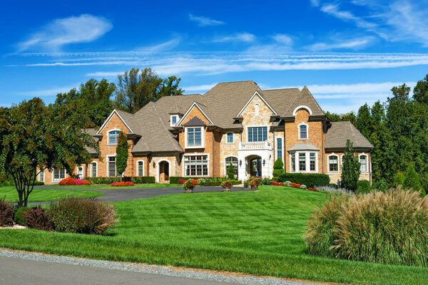 Large brick country house for one family with beautiful landscaping and lawn. Summer landscape on a sunny day under a blue sky.