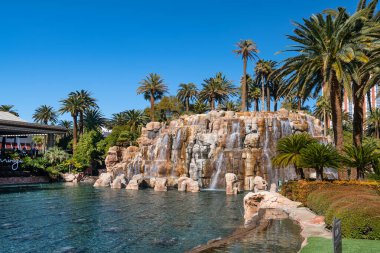 Las Vegas, Nevada 'da, Strip' teki Mirage Otel ve Kumarhanesinin yanında palmiye ağaçları olan bir şelale ve gölet..