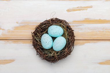 Twig nest and easter eggs on a white wooden table. View from above. Space for text.