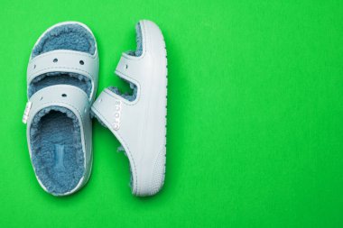 blue branded Crocs sandals on green background. Top view, space for text.