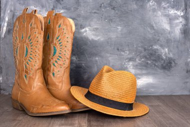  Leather cowgirl boots with a pattern and a hat stand on the floor against a gray wall. Space for text.