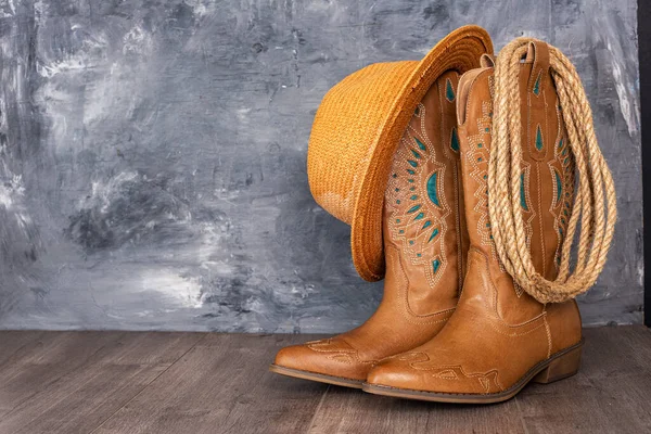 Leather cowgirl boots with pattern and hat stand on the floor against gray wall. Space for text.