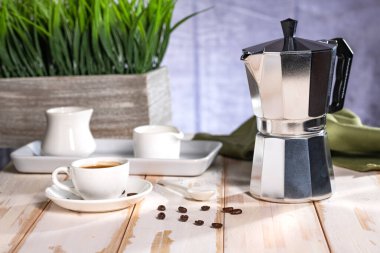 Italian geyser coffee maker and ceramic coffee cup on white table in the room.