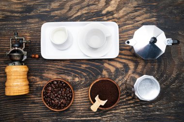 classic manual aluminum geyser coffee maker, vintage manual coffee grinder and porcelain tableware for coffee drinking on a dark wood background. view from above.