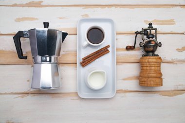classic manual aluminum geyser coffee maker, vintage manual coffee grinder, and porcelain tableware for coffee drinking on wood table. View from above