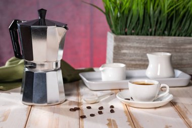 Italian geyser coffee maker and ceramic coffee cup on white table in the room.