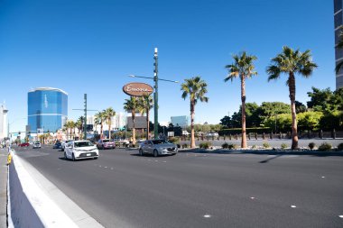 main street of Las Vegas with hotels walking areas and traffic. Palm trees against the blue sky.