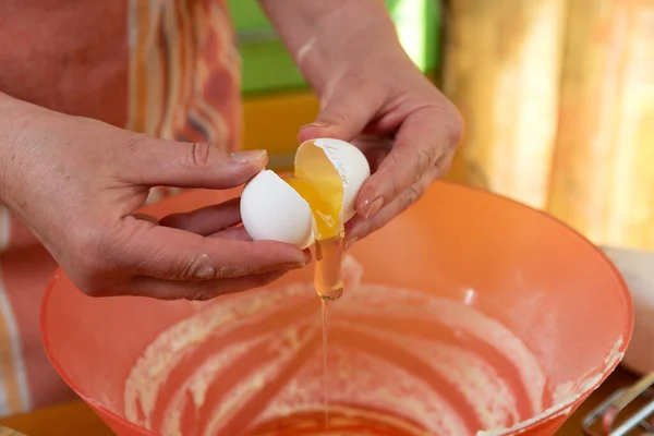 hostess in an apron extracts the yolk from a raw egg into a bowl of flour to make dough. ingredients for cooking on the countertop