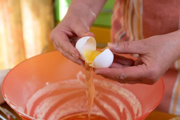 hostess in an apron extracts the yolk from a raw egg into a bowl of flour to make dough. ingredients for cooking on the countertop
