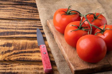 Koyu ahşap arka planda taze domates ve kesme tahtasındaki bir bıçak. Domates hasadı. Metin için boşluk.