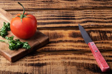 Koyu ahşap arka planda taze domates ve kesme tahtasında bir bıçak. Domates hasadı. Metin için boşluk.