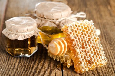 İki kavanoz bal, bir kepçe ve ahşap desenli masada bal peteği.