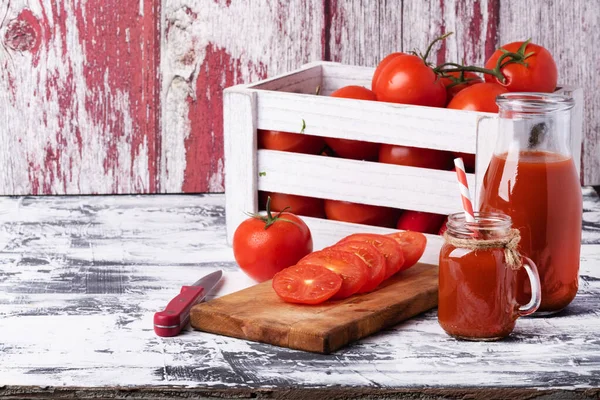 把新鲜的西红柿放在木箱里 把西红柿片放在切菜板上 把一瓶番茄汁放在白桌上 — 图库照片