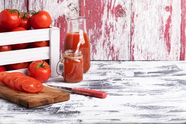 木の箱で新鮮なトマトを熟す まな板にトマトスライスと白いテーブルの上にトマトジュースのボトル — ストック写真