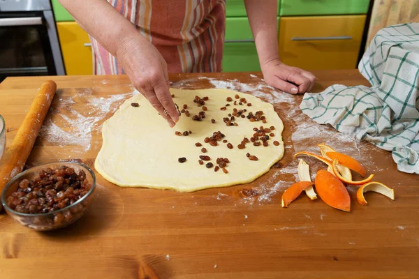 厨师的手在生面团里放葡萄干以便在家里厨房里做甜馅饼 — 图库照片