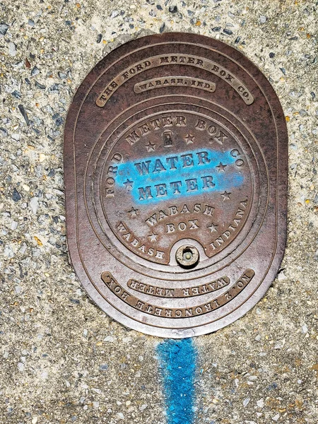 stock image Metal cover of the water meter on the sidewalk. The name of the company and state of the manufacturer. View from above.