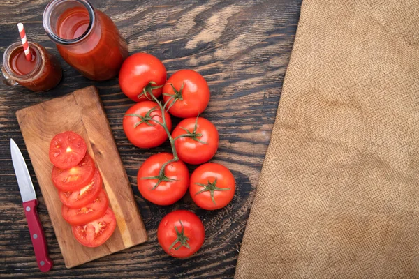 大きな熟したトマトとスライスを切ったボード上でまだ生きています 瓶の中のトマトジュース 暗いテーブルとバラップ 上からの眺め テキストの場所 — ストック写真