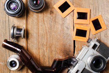 Klasik fotoğraf makinesi, lensler, negatifler ve slaytlar desenli ahşap bir masada. Yukarıdan bak. Eski tarz. Metin için boşluk.
