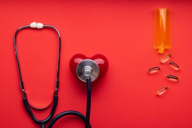 Stetoskop, haplar ve kırmızı arka planda kırmızı kalp, üst manzara. Metin için boşluk.