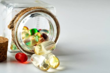 Beyaz bir masada ilaç ve vitaminlerle çevrilmiş cam ilaç şişesi. Yakın plan. Metin için boşluk.