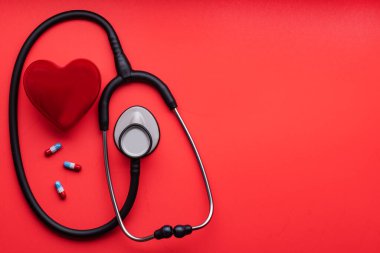 Tıbbi steteskop, kırmızı kalp ve kırmızı arka planda haplar. Yukarıdan bak. Metin için boşluk