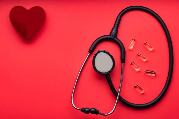 medical stethoscope, red heart and pills on a red background. View from above. Space for text