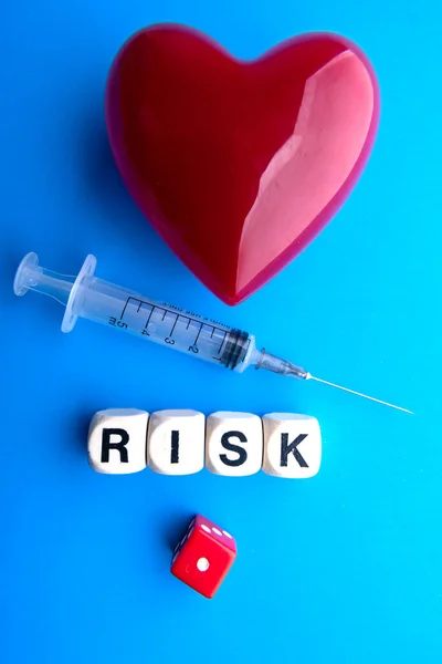 Red heart and syringe on a blue background. Wooden cubes with the inscription RISK. Health and immunity concept