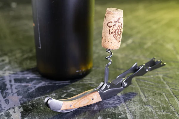 コルク抜きとワインボトルのクローズアップ 古い黒いテーブルの上のオープンボトル — ストック写真