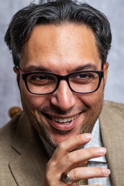 Gözlüklü, gülümseyen siyah saçlı adam. Ceket ve kravat. Yakın plan..