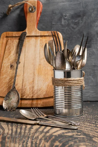 老式叉子 刀叉和勺子放在黑暗的木制桌子上的铁罐里 切割板 灰色背景 文字空间 — 图库照片