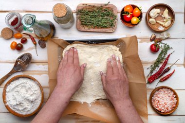 Kadın aşçı, İtalyan Focaccho ekmeği yapmak için hamuru bir yemek tepsisine serer. Un ve malzemeler. Yukarıdan görüntüle.