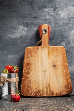 Kiraz domatesli teneke kutu ve gri bir duvara karşı koyu ahşap bir masanın üzerinde bir kesme tahtası. Metin için boşluk.